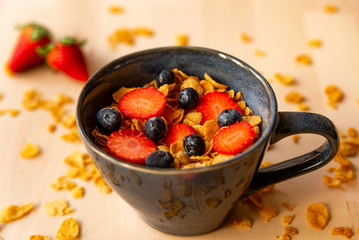 closeup of healthy corn flakes breakfast bowl on wooden table with corn flakes, strawberries and blueberries and fruit with natural light