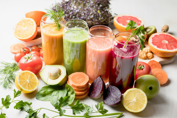 freshly squeezed juice, fruit and vegetable smoothies in glass glasses on a white table decorated with a composition of fruit
