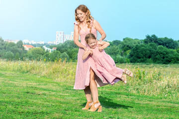 Portrait of beautiful happy mother and daughter hugs and playing in outdoor park together