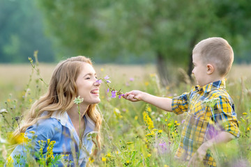 Beautiful baby boy child with young mother wearing casual clothes outdoors picking flowers in a summer meadow