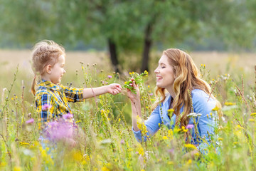 Beautiful baby girl child with young mother wearing casual clothes outdoors picking flowers in a...