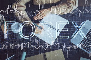 Forex graph on hand taking notes background. Concept of research. Double exposure