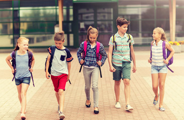 primary education, friendship, childhood, communication and people concept - group of happy elementary school students with backpacks walking and talking outdoors