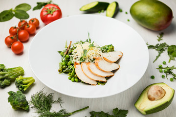 fresh vegetable salad light chicken salad on a large white plate on a white table with a composition of tomatoes, avocado, parsley, cucumber, peas, broccoli
