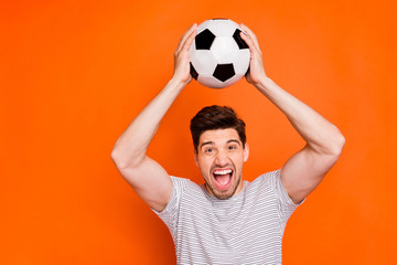 Photo of attractive crazy guy hold football leather ball hands above head supporting team watch television wear striped t-shirt isolated bright orange color background