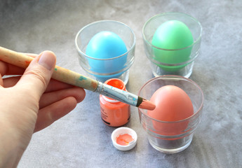 Coloring Easter eggs. A wooden brush with an orange paint in the woman's hand, an open jar of paint, and painted eggs in pastel colors. Selective focus
