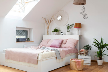 Cozy bedroom in white and pink color with comfortable bed and pink pillow. Scandinavian interior in apartment with stylish decoration. 