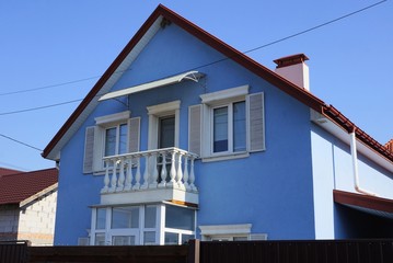 large blue private house with a white balcony and windows behind a brown fence against the sky