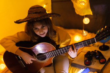Obraz premium Little girl playing acoustic guitar under the tent in a living room.