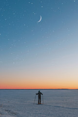 Man standing on snow coverd open with skis on foot with beautiful starry sky and moon.