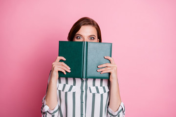 Close up photo of astonished crazy girl hide her lips mouth read book learn incredible lecture encyclopedia information wear modern clothing isolated over pink color background