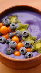 Smoothies of violet color from banana and currant, on top of a blackberry, physalis and kiwi berry. Smoothies in a wooden bowl.