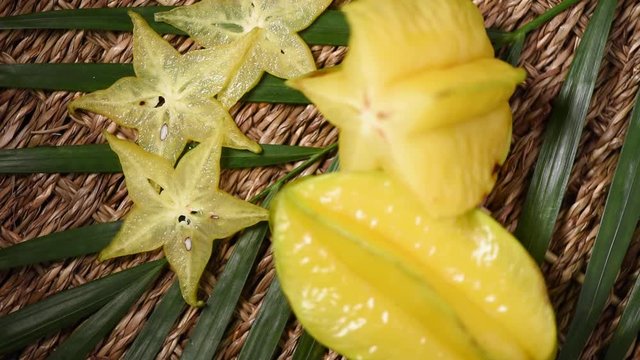 Yellow carambola fruit on rotating background. Top view. Exotic fruits, tropical palm branch. Vegan and raw food concept.