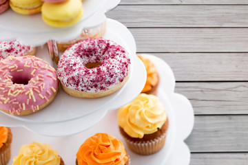 fast food, dessert and sweets concept - close up of glazed donuts and cupcakes on stand over grey wooden boards background