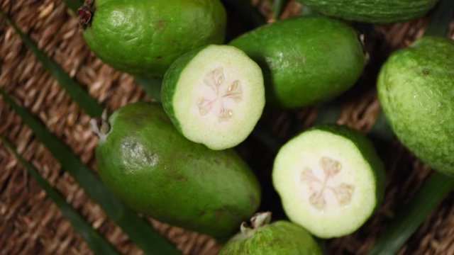 Green feijoa fruits on rotating background. Top view. Exotic fruit, tropical palm branch. Vegan and raw food concept.