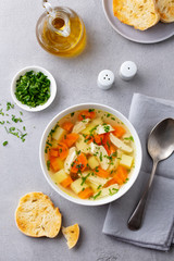 Chicken soup with vegetables in white bowl. Grey background. Top view.