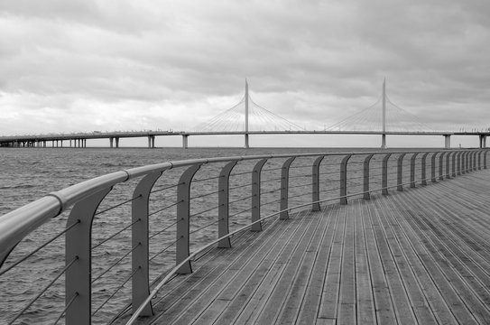 Landscape photograph of the river embankment or seafaring flooring of wooden boards and view of the car overpass on a cloudy day. Black and white. Selective focus. Horizontal orientation.