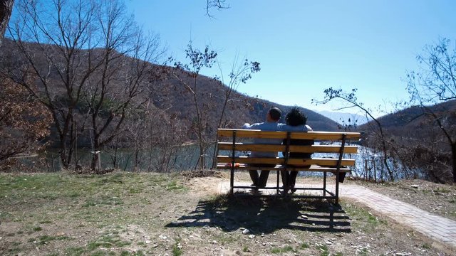 sweet romantic couple sitting an hugging on bench in the park with view to the lake
