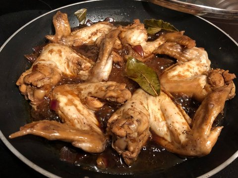 Chicken wings cooked adobo style in a pan, with bay leaves