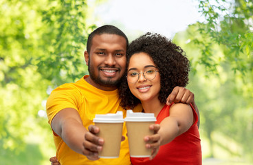 relationships and people concept - happy smiling african american couple with takeaway coffee cups over green natural background