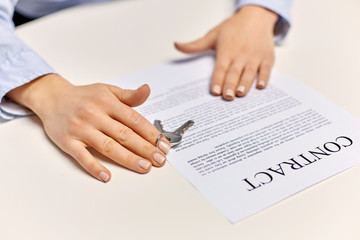 real estate business and people concept - close up of businesswoman or realtor's hands with keys and contract on table