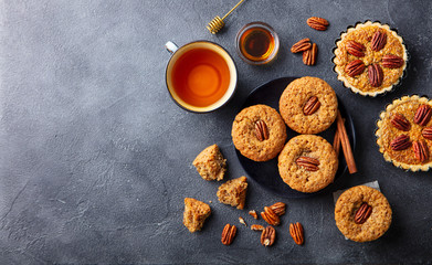 Pecan muffins, cakes, pies with cup of tea. Dark background. Top view. Copy space.