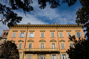 Obraz premium Orange apartment with shutters in street with trees, called Via S Giovanni del Cantone. Modena, Italy.
