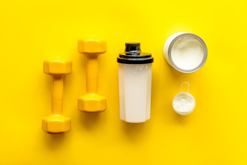 Sport nutrition. Whey protein, shaker, dumbbells on yellow background top-down flay lay
