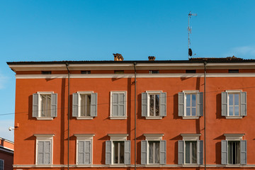 Fototapeta na wymiar Orange building with white shutters on square Piazza Roma. Modena, Italy