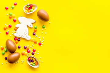 Sweet Easter symbols - chocolate eggs and bunny gingerbread - on yellow background top-down frame copy space
