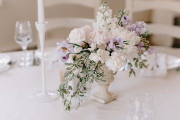 Wedding banquet table setting. Plates, glasses, cutlery and flower arrangement on a white round table. Round table with a white tablecloth. Plate with a gray cloth napkin.