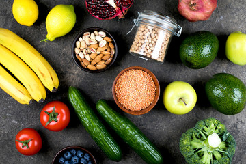 Healthy vegan food diet concept. Green vegetables, tomatoes, nuts and fruits on dark concrete table. Flat lay, top view