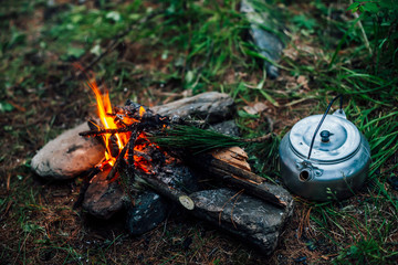 Camping kettle near small camp fire close-up. Cozy camping place in wild. Wonderful evening atmospheric background of campfire. Beautiful flame of small magic bonfire. Romantic warm place with fire.