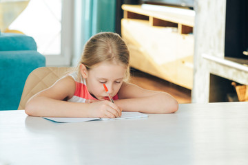 Obraz na płótnie Canvas little girl at the table with a notebook, doing homework.