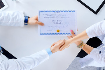 Doctor congratulates intern on receiving diploma and shakes hands in hospital