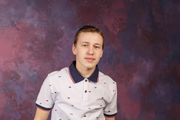 a young man in a white t-shirt with a blue collar, taken by the light of a softbox against a multicolored wall