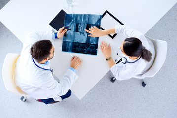 Medical team of doctors sitting and discussing about x-ray at table with tablets, top view