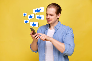 A man in a shirt on a yellow background looks like in a smartphone. Abstract icons with thumb up hanging in the air.