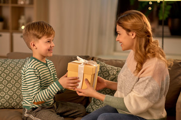 mother's day, holidays and family concept - happy little son giving present to his mother at home in evening