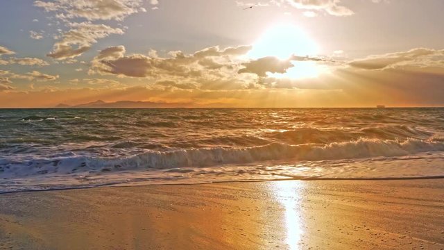 Beautiful orange sunlight shining on the beach; fix shot of churning surf; beautiful sun above the sea surface