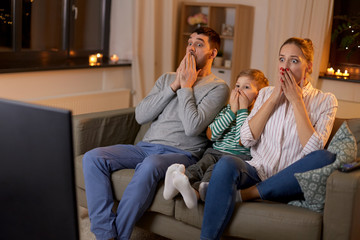 family, leisure and people concept - scared father, mother and little son watching tv at home at night