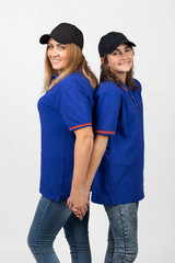 Two different-aged girls of European appearance in the same clothes stand with their backs to each...