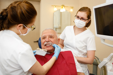 Young female dentist is looking whether ceramic veneer fits tooth of senior man