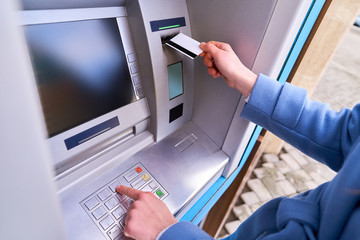 Person insert plastic credit card into atm bank and dials a PIN code on the keyboard to withdrawing...