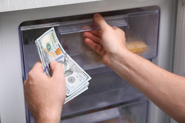 Man hiding money in refrigerator, closeup. Financial savings