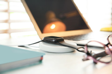 Obraz premium Smartwatch with wireless charger on white wooden table. Modern workplace accessory