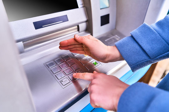 Person dials and hides with other hand for security purposes a PIN code on the keyboard of atm bank to withdraw cash