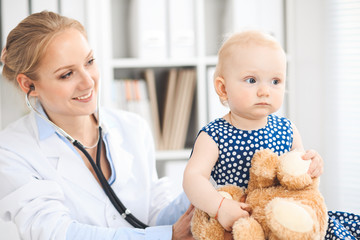 Doctor and patient in hospital. Little girl dressed in dark blue dress is being examined by doctor with stethoscope. Medicine and healthcare concept