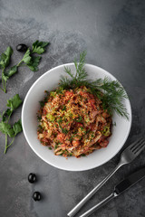 top view salad of vegetables, olives and shrimp sprinkled with sesame seeds on white plate, grey background in rustic style with copy space