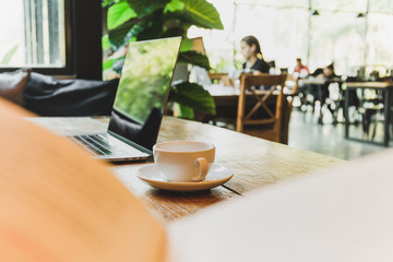Selective focus on coffee cup and laptop on wooden table with blurbackground.